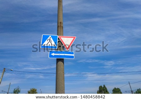 Road sign - Pedestrian crossing. Square plate with stripes and walking man. Road sign - Give way. White triangle with a red border. Road sign - Direction of movement. White arrow on a blue rectangle