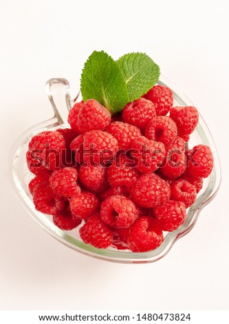 Bright raspberries in a vase in the shape of an apple on a white background, top view.