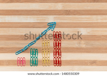 An arrow siting on a bunch of paperclips arranged in columns on a brown table, shot from above.
