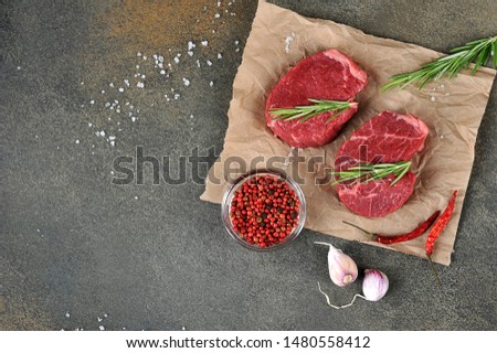 Two raw beef steaks on paper. Rosemary, garlic, pepper and grilled steak salt. Dark background. Top view. Free space for text.