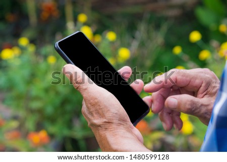 Close-up of wrinkled hands senior man holding a smartphone in the garden