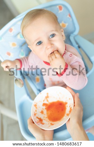 Adorable cute caucasian blond toddler boy eating tasty vegetable soup in chair at kithcen indoor. Mother feeding baby healthy food with spoon. Natural children nutriotion and diet