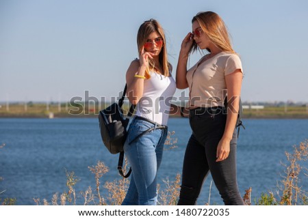 two beautiful young and stylish girl sitting in a summer city near water. Portrait.