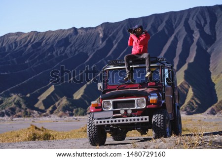 Traveller sit and take a photo on a vintage off road car with Bromo mountain background