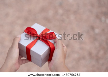 Hand holding sliver gift box with red ribbon on ground blurred 