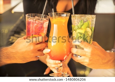 Hands with tropical cocktails at  party. Young people drinking cocktails, summer vacation concept.  Focus on bottom hands glass - Image