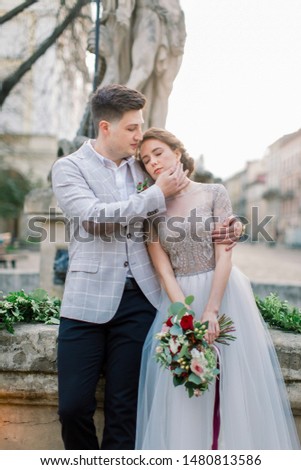Close-up portrait of romantic young wedding couple embracing each other while standing on the old stone stairs in city center