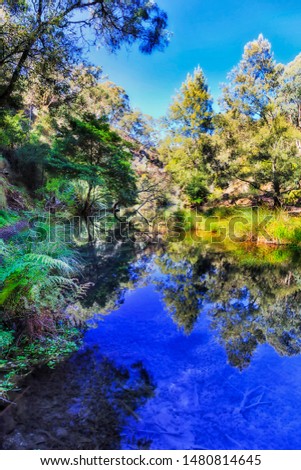 Calm still waters of BLue lake on Jenolan river near Jenolan caves in Blue Mountains of Australia on a sunny day with lush vegetation on shores reflecting in water.