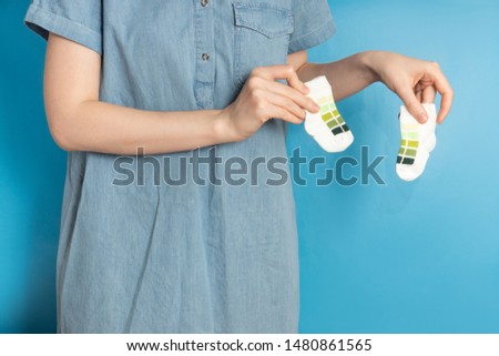 Woman holds little baby socks on blue background