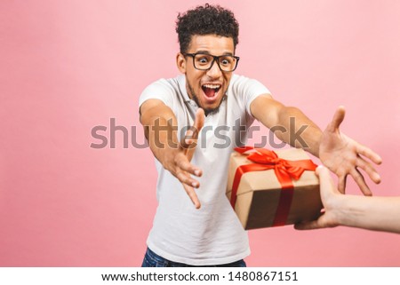 Cheerful smiling african american millennial guy in eyewear holding wrapped present box. Happy black young man congratulating, giving birthday gift, isolated on pink background.