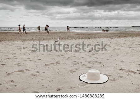 Adriatic coast. Straw hat on the sand. Seagull. Unrecognizable  People walking after the storm.