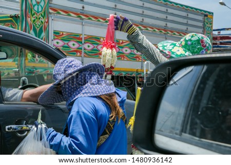 The seller walks the garland of flowers And food for the car parked on the road That is the crossroads between cars stopped waiting for signal lights.
