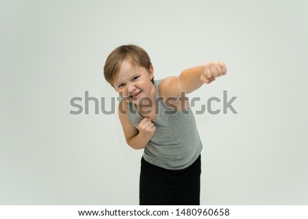 Photo is a waist-high portrait of a fun cheerful cute happy school-age athlete boy in a T-shirt. Rejoices, smiles on a white background. Shows hands.
