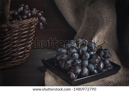 still life with black grapes and a basket on burlap, rustic style, low key