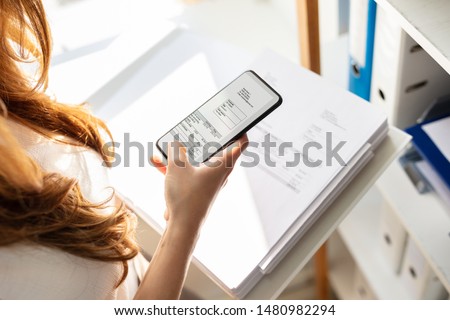 Young Businesswoman Taking Photograph Of Invoice Document Secretly In Office