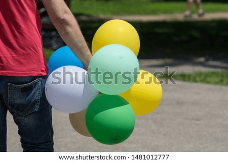 Hand of a man holding colourful balloons in the air, on green, yellow and blue, on blurred outdoor background
