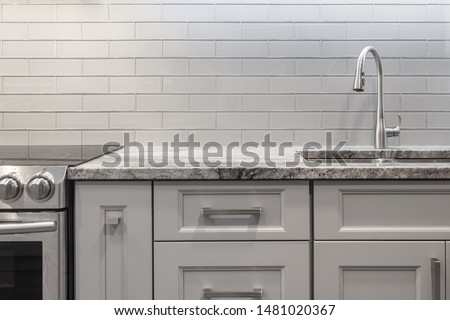 Brushed nickel faucet, stainless steel sink, granite countertop, white and grey tones. grey subway glass tile backsplash, glass top stove, stainless steel oven  Royalty-Free Stock Photo #1481020367