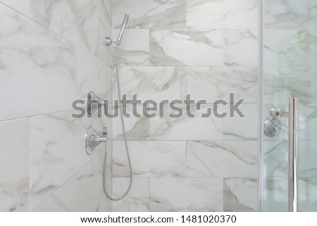 Shower with marble looking porcelain tiles, frameless glass shower door, polished chrome shower fixtures, hand held shower head Royalty-Free Stock Photo #1481020370