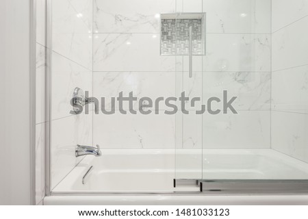 White marble, granite looking porcelain tiles polished surface bathtub and shower with niche and glass shower doors Royalty-Free Stock Photo #1481033123