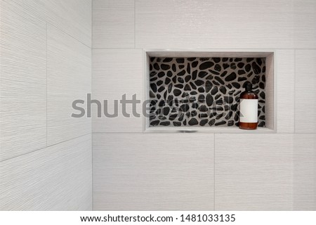 Shampoo / shower gel bottle in a rectangular niche made of black pebble mosaic tiles in shower and bathroom. Brown shampoo bottle with white sticker Royalty-Free Stock Photo #1481033135