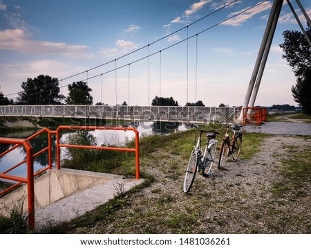 Retro bicycles on a gravel road. In the background is a white suspension bridge. Bicycles represent a two-wheeled adventure journey. Retro style picture.