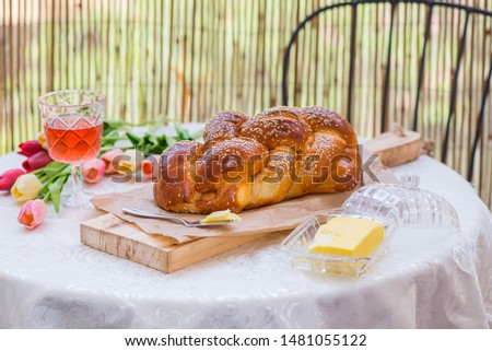 Challah bread on round table served with Amber wine in a glass and butter , with flowers on background , Shabbat time 
