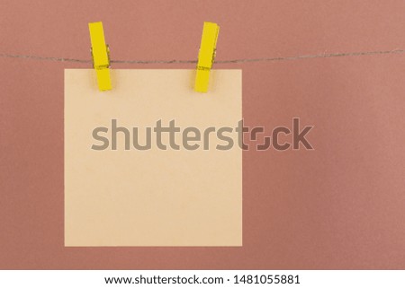 paper sheets of a notebook for notes and reminders of beige color fastened with decorative yellow clothespins hang on a rope on a brown background