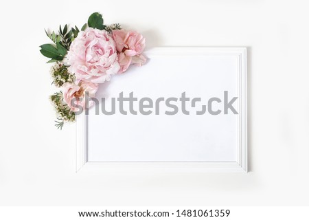 Wedding, birthday sign board mock-up scene. Blank white wooden frame. Decorative floral corner. Green leaves, pink peony, roses and wax flowers. White table background. Flat lay, top view.
