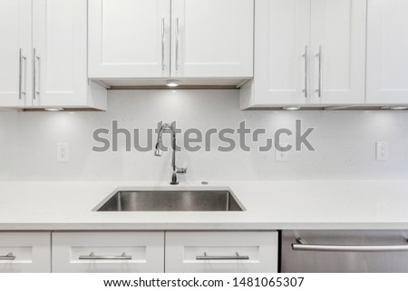 White kitchen built with shaker style cabinets and white granite. Shows stainless dishwasher, granite back splash. Brushed chrome faucet and hardware
 Royalty-Free Stock Photo #1481065307
