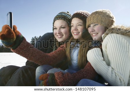 Three female friends taking self portrait through cell phone in winter