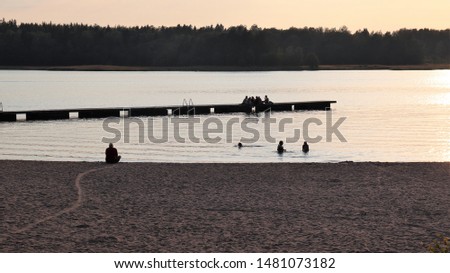 Silhouettes of people enjoying the warm summer evening by swimming, sitting on the beach and spending time on the duck.