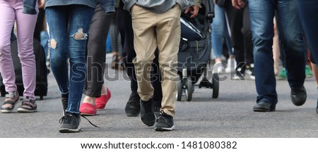 A big group of people walking to the same direction in the train station. In front, there is a young person with broken jeans and another one with brown trousers. Selective focus. Royalty-Free Stock Photo #1481080382