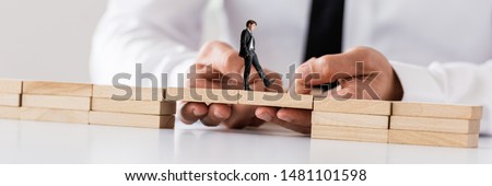 Businessman making a bridge between two stacks of wooden pegs for another businessman to walk safely across in a conceptual image. Royalty-Free Stock Photo #1481101598