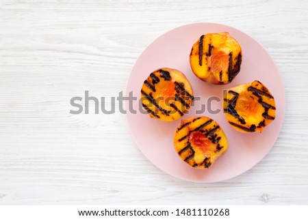 Homemade grilled peaches on a pink plate on a white wooden background, top view. Flat lay, overhead, from above. Copy space.