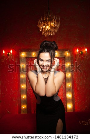 Cheerful young woman wearing party dress in red fashion room with light bulbs