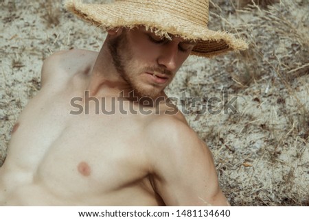Strong face male model in casual wear with hat on the nature background with sand and water and trees on the beach on the sunset
