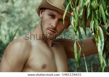 Strong face male model in casual wear with hat on the nature background with sand and water and trees on the beach on the sunset