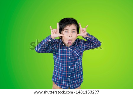 Image of little boy taunting someone while sticking out tongue in the studio with green screen Royalty-Free Stock Photo #1481153297