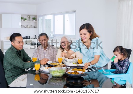 Picture of happy woman serving foods for her multi generation family while having lunch together at home