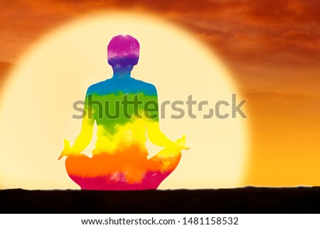 Picture of a young woman meditating in lotus pose with colorful chakra within her body at sunset time