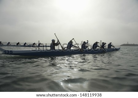 Group of multiethnic people paddling outrigger canoes in race Royalty-Free Stock Photo #148119938