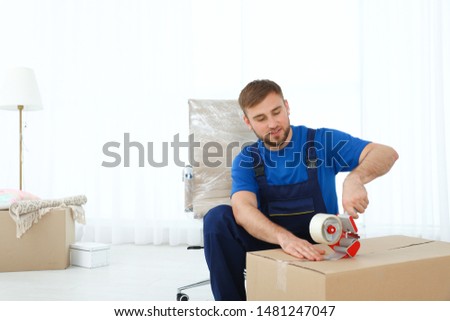 Young worker packing box in room. Moving service