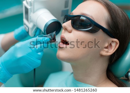 Dentist takes jaw x-ray. Patient in dental chair. Dentist's hands with blue gloves work with a dental tools. Beautiful young woman having dental treatment.