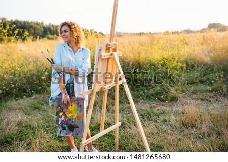 Pretty talented female painter painting on easel, making colorful sketches, creating marine landscape. Beautiful female artist painting with watercolor paints. Creativity and imagination concept.
