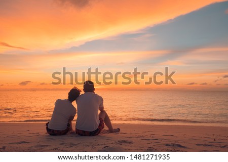 Couple in love watching sunset together on beach travel summer holidays. People silhouette from behind sitting enjoying view sunset sea on tropical destination vacation. Romantic couple on the beach Royalty-Free Stock Photo #1481271935