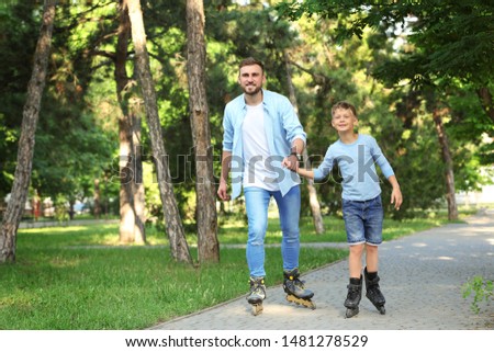 Father and son roller skating in summer park