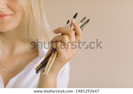 Close up artist holding paint brushes against beige background. Modern minimalist creative blog concept. Copy space.