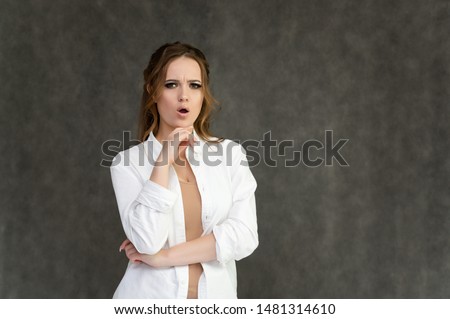 Photo waist-length portrait of a pretty brunette woman girl with long beautiful curly hair on a gray background in a white shirt. Talking in different poses. Standing facing the camera.