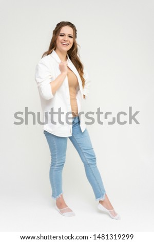 Photo full-length portrait of a pretty brunette woman girl with long beautiful curly hair on a white background in a white shirt and blue jeans. Talking while standing in front of the camera.