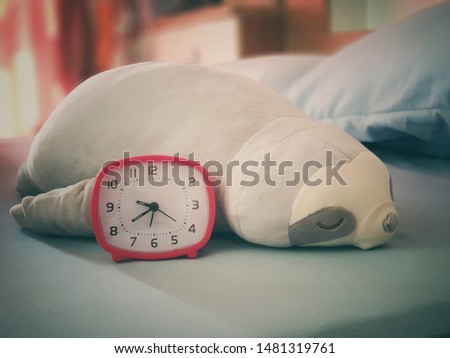A doll sloth with a red alarm clock on the bedroom to wake up late and still sleeping 